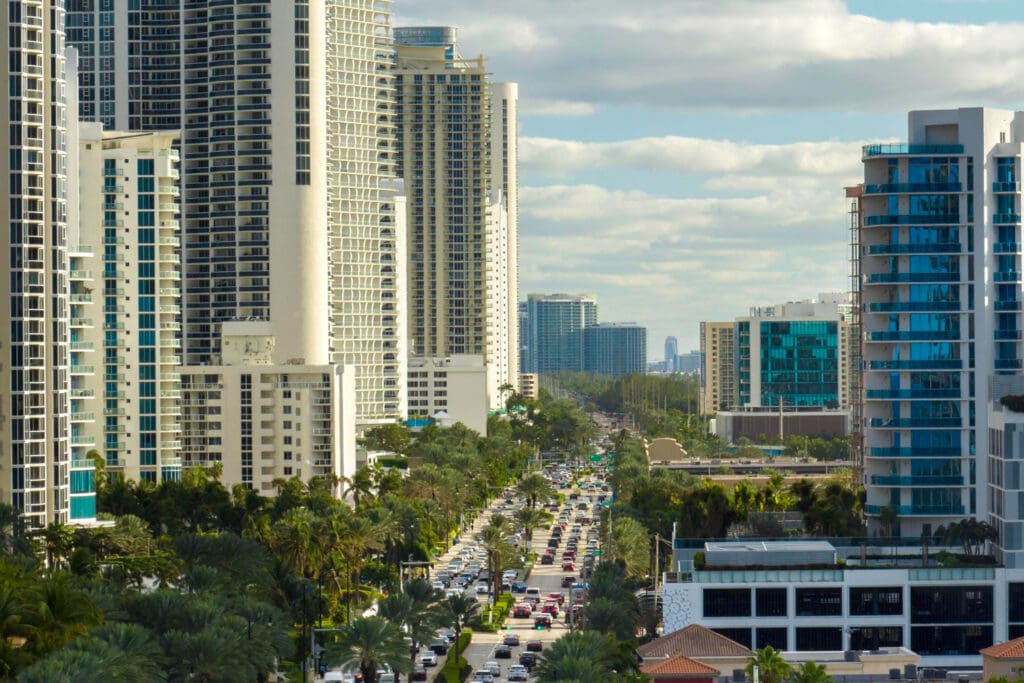 An aerial view of a busy street with congested traffic in Sunny Isles Beach, Florida, surrounded by numerous modern high-rise condominium and hotel buildings.