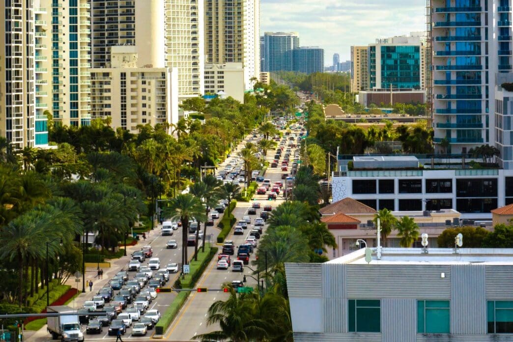 An aerial view of a busy street with congested traffic in Sunny Isles Beach, Florida, with a dense skyline of high-rise condos and hotels.