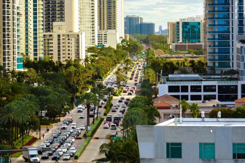 An aerial view of a busy street with congested traffic in Sunny Isles Beach, Florida, with a dense skyline of high-rise condos and hotels.