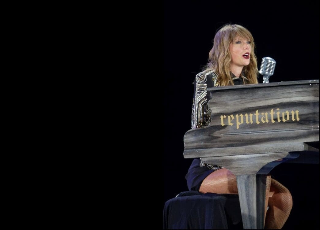 Taylor Swift plays a black piano with the word "reputation" written on it