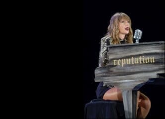 Taylor Swift plays a black piano with the word "reputation" written on it