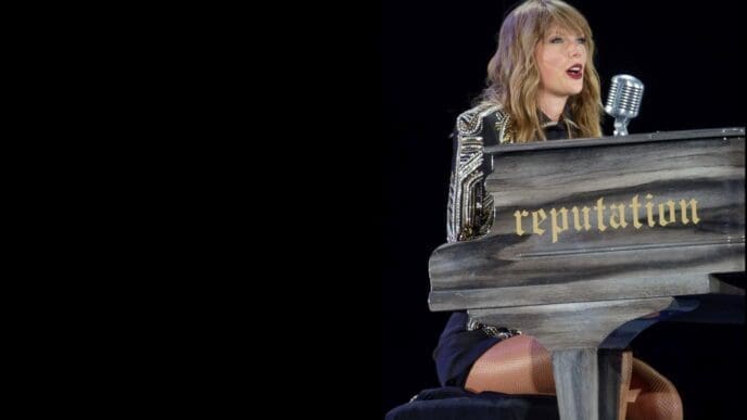 Taylor Swift plays a black piano with the word "reputation" written on it