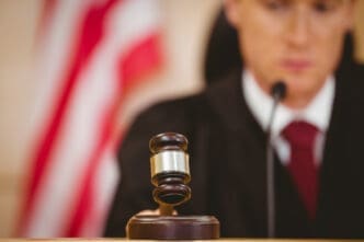 A gavel resting on a sound block with a judge in the background.