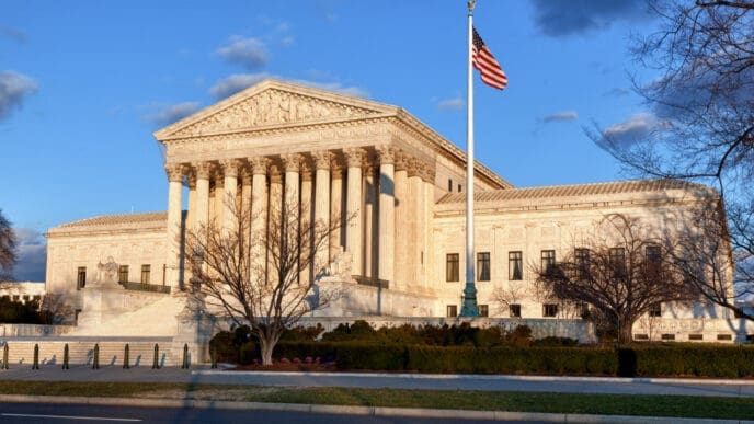 A photograph of the Supreme Court of the United States building, a white neoclassical structure with a grand staircase and columns, with an American flag flying in front of it.
