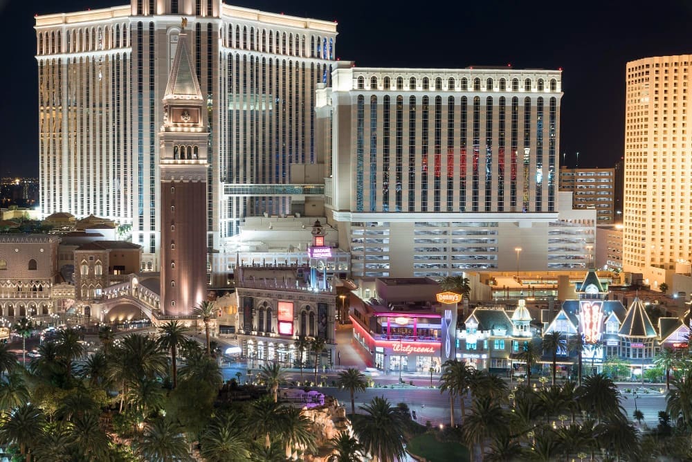 A nighttime view of the Venetian Resort in Las Vegas, showing the bell tower and bright lights of the city and its buildings.