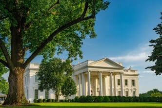 The White House is visible on a sunny day with lush green trees in the foreground.