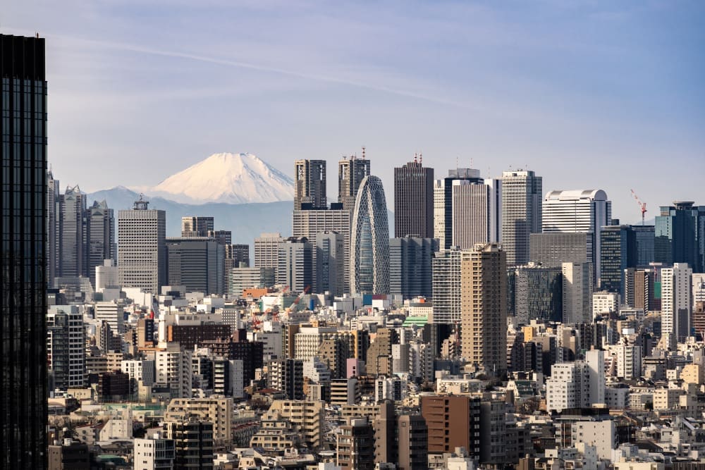 The skyline of Tokyo is seen with numerous financial buildings and the snow-capped Mount Fuji in the background.