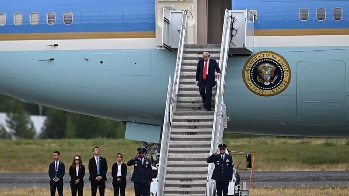 President Donald Trump disembarks from Air Force One, walking down the stairs past a line of officials and military personnel in Alaska.