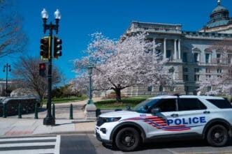 A police car parked in front of the U.S. Capitol building, with a cherry blossom tree in full bloom and a traffic light in the foreground.