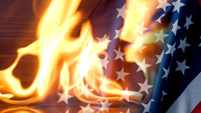 A photograph of the American flag, with its stars and stripes, is engulfed in bright orange and yellow flames.
