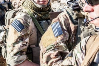 A close-up shot of two U.S. Army Rangers in camouflage uniforms with American flag patches and tactical gear.