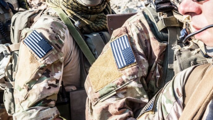 A close-up shot of two U.S. Army Rangers in camouflage uniforms with American flag patches and tactical gear.