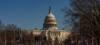 The U.S. Capitol building stands behind a street with traffic lights and bare trees