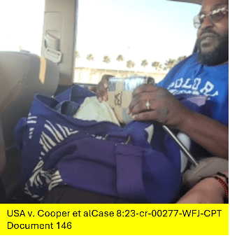 Virgil Cooper, sitting in a car, is shown in a candid photograph holding a cardboard box over a purple duffel bag.