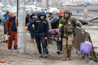 A group of people, including a soldier, carries a stretcher with an injured person through a muddy street during the war in Irpin, Ukraine.