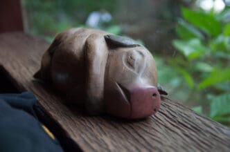 A close-up of a small, carved wooden pig figurine with a pink nose, lying on a wooden windowsill.