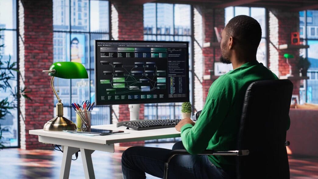 An African American engineer works on visual coding on a computer terminal in a home office.