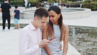 A young African woman looks upset while her boyfriend is focused on his smartphone.
