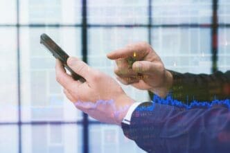 A person uses a smartphone to analyze financial data related to a business and trading.