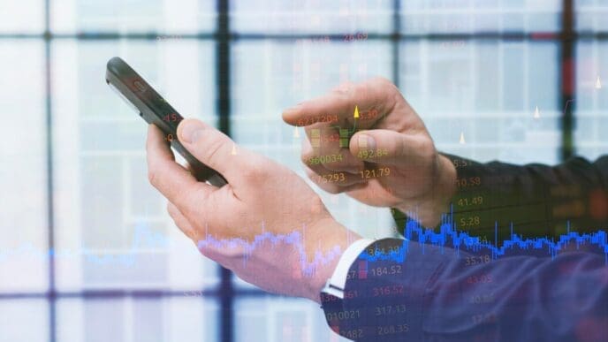 A person uses a smartphone to analyze financial data related to a business and trading.