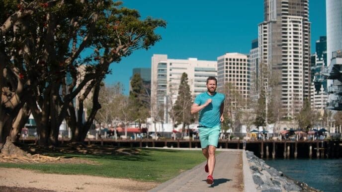 A young man runs through a city on a sunny day.