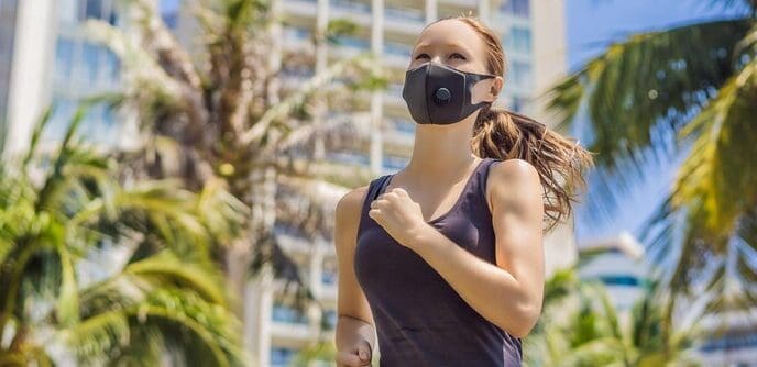 Woman wearing a medical mask runs in a city, with buildings in the background.