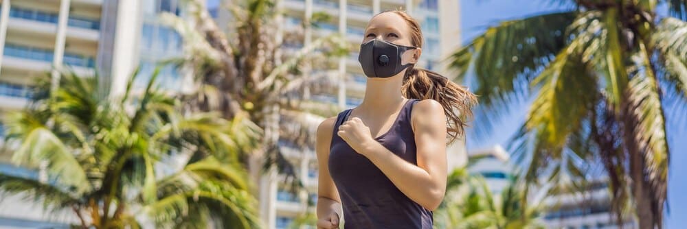 Woman wearing a medical mask runs in a city, with buildings in the background.
