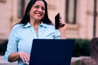 A smiling, mature Latina woman works on a computer in her backyard.