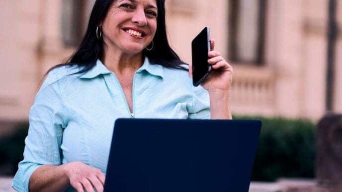 A smiling, mature Latina woman works on a computer in her backyard.