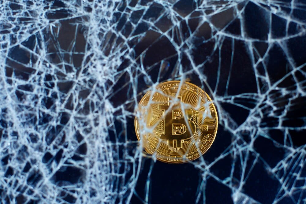 Cracked glass with a Bitcoin logo symbolizes the cryptocurrency's crash and collapse.