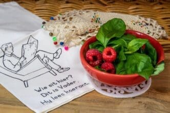 Close-up of a bowl filled with fresh red raspberries and green basil leaves.