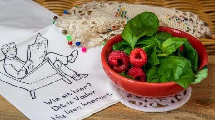 Close-up of a bowl filled with fresh red raspberries and green basil leaves.