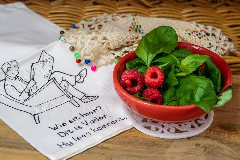 Close-up of a bowl filled with fresh red raspberries and green basil leaves.
