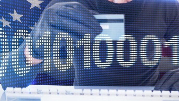 A person is using a laptop and credit card to make an online purchase, with binary code displayed on the screen.