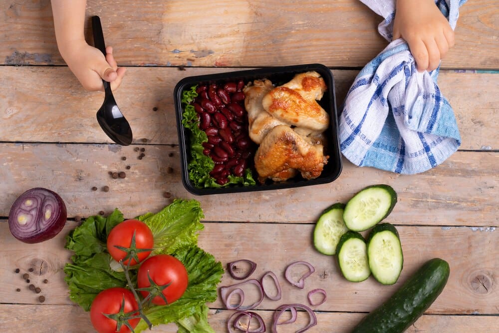 A business lunch in food boxes features roast chicken wings, steamed vegetables, and stewed meat, offering a ready-to-eat meal.