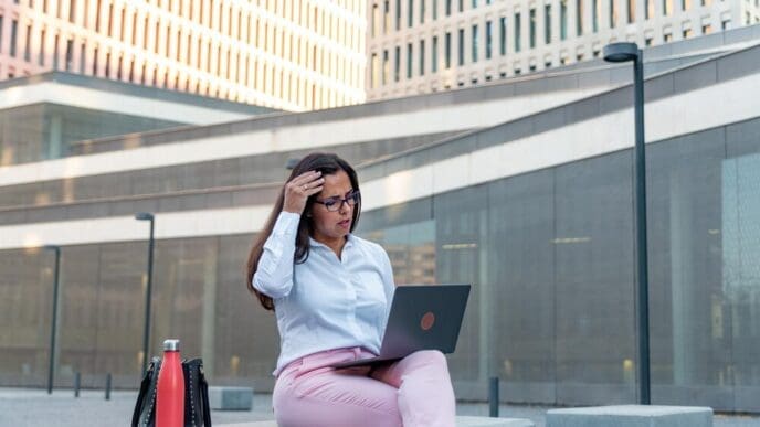 A businesswoman works on a laptop while seated outside.