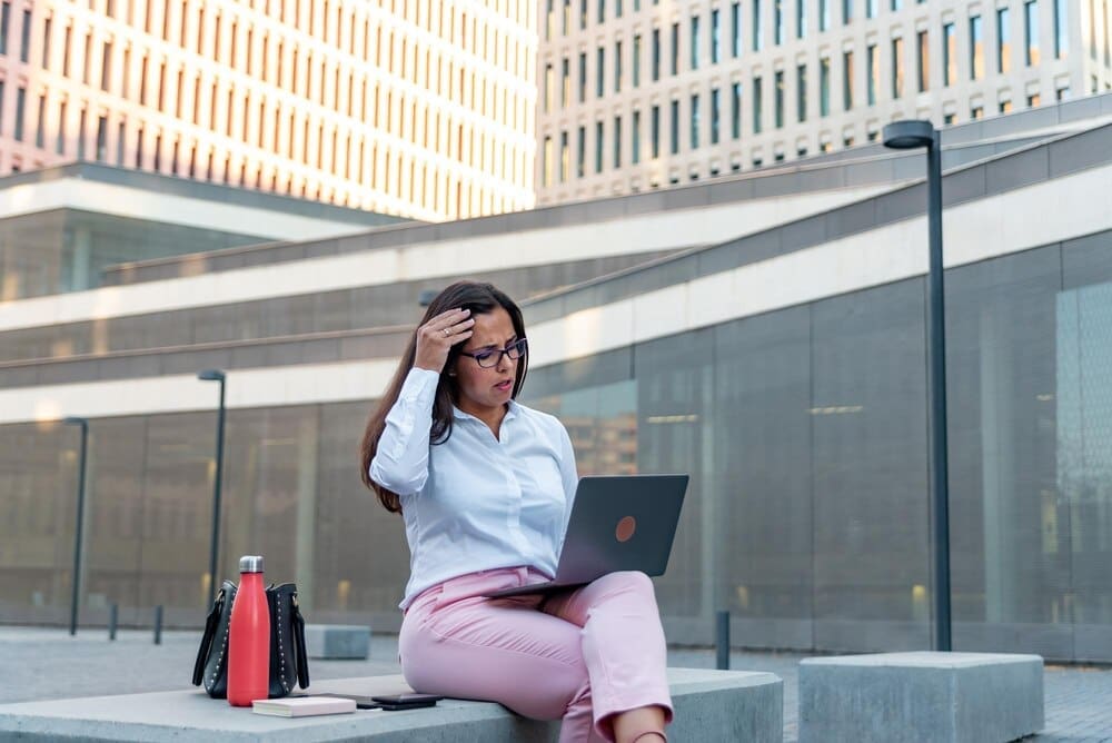 A businesswoman works on a laptop while seated outside.