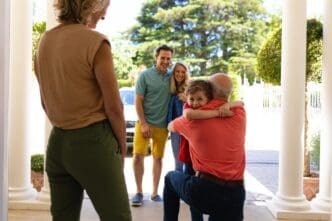 A mature Caucasian woman and a mid-adult couple watch as a young boy hugs an elderly Caucasian man.