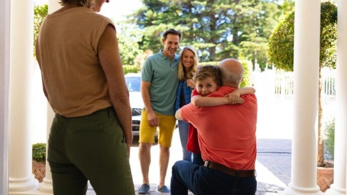 A mature Caucasian woman and a mid-adult couple watch as a young boy hugs an elderly Caucasian man.