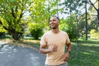 A smiling Hispanic man jogs through a sunny park.