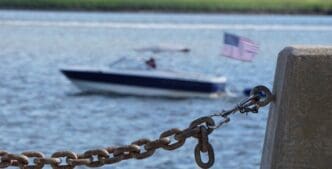 Close-up of a boat's chain connecting it to a mooring on the shore.
