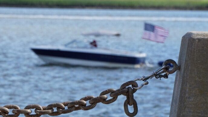 Close-up of a boat's chain connecting it to a mooring on the shore.
