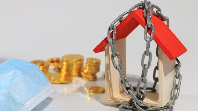 Close-up shows text and numbers superimposed over toy blocks in front of a model home, with a chain and white background.