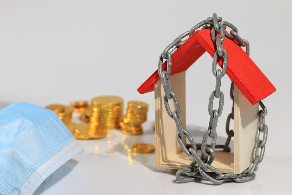Close-up shows text and numbers superimposed over toy blocks in front of a model home, with a chain and white background.