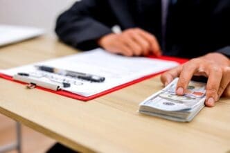 Close-up of fingers touching a bundle of US dollar bills next to a legal document, possibly suggesting a bribe.