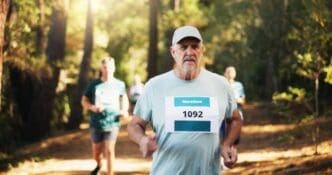 A mature man runs a marathon in a forest.