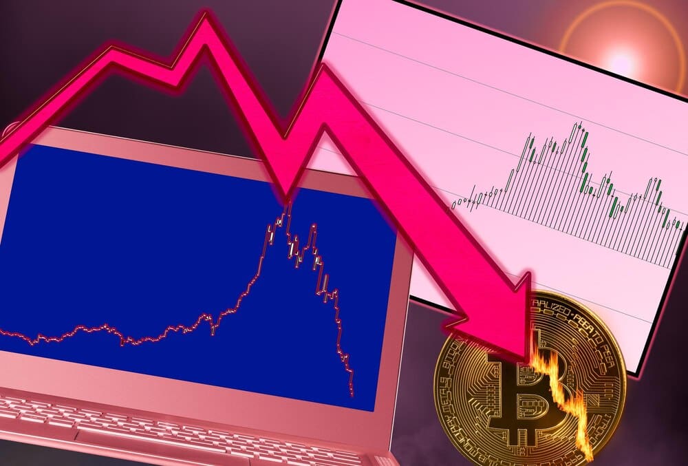 A laptop displays a graph of falling prices, with a flaming bitcoin symbol superimposed, illustrating a price crash for cryptocurrency.