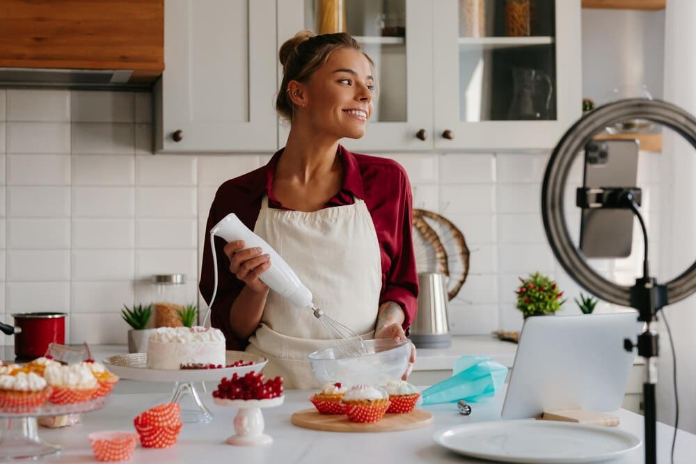 A female pastry chef confidently whisks cream while preparing a cake in a home kitchen.