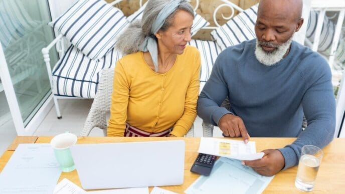 A couple sits at a table, reviewing financial documents and using a calculator.