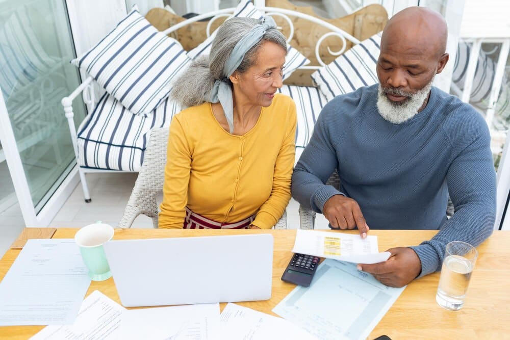 A couple sits at a table, reviewing financial documents and using a calculator.